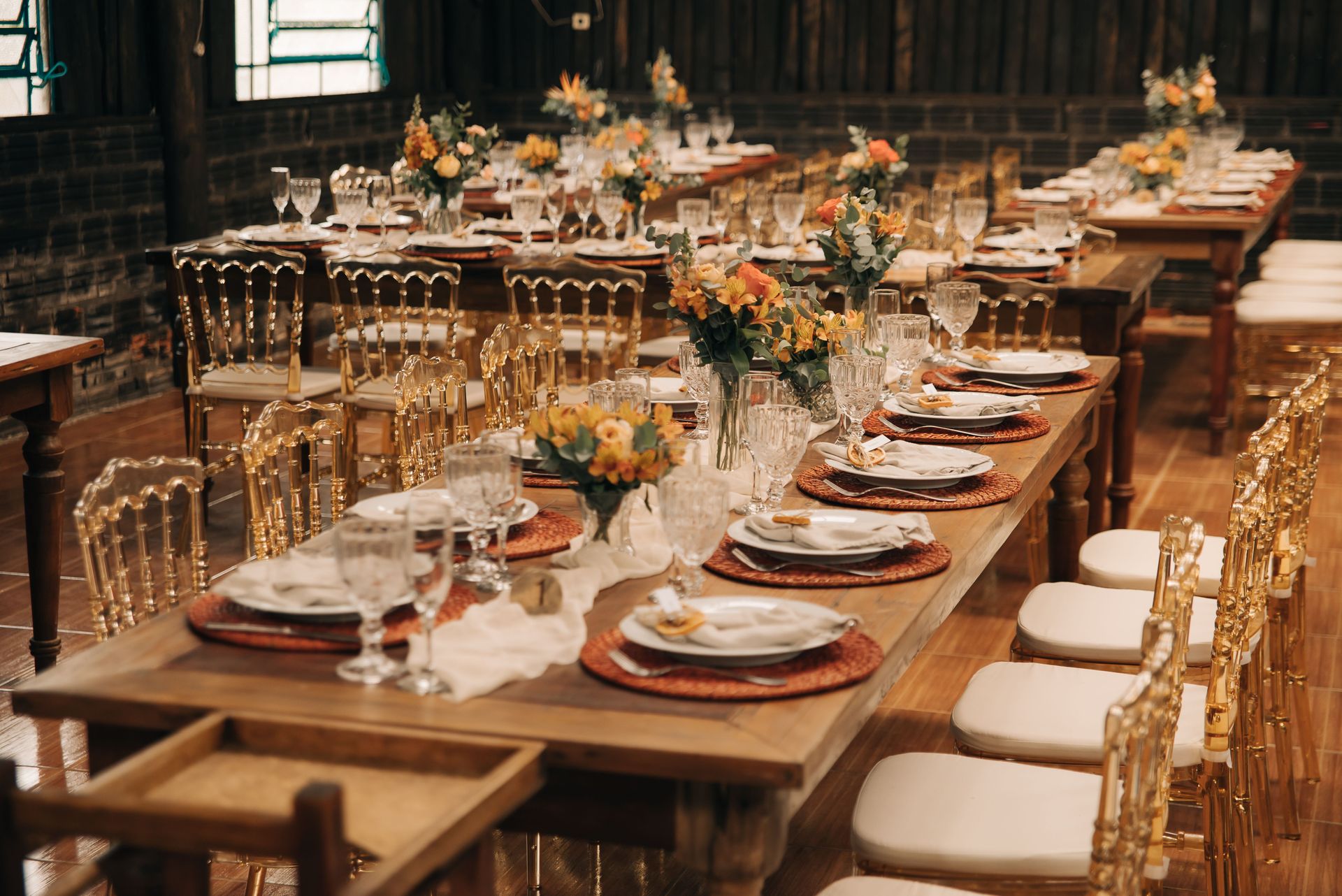 Chic wedding banquet setup with flowers, plates, and crystal glasses on long wooden tables.