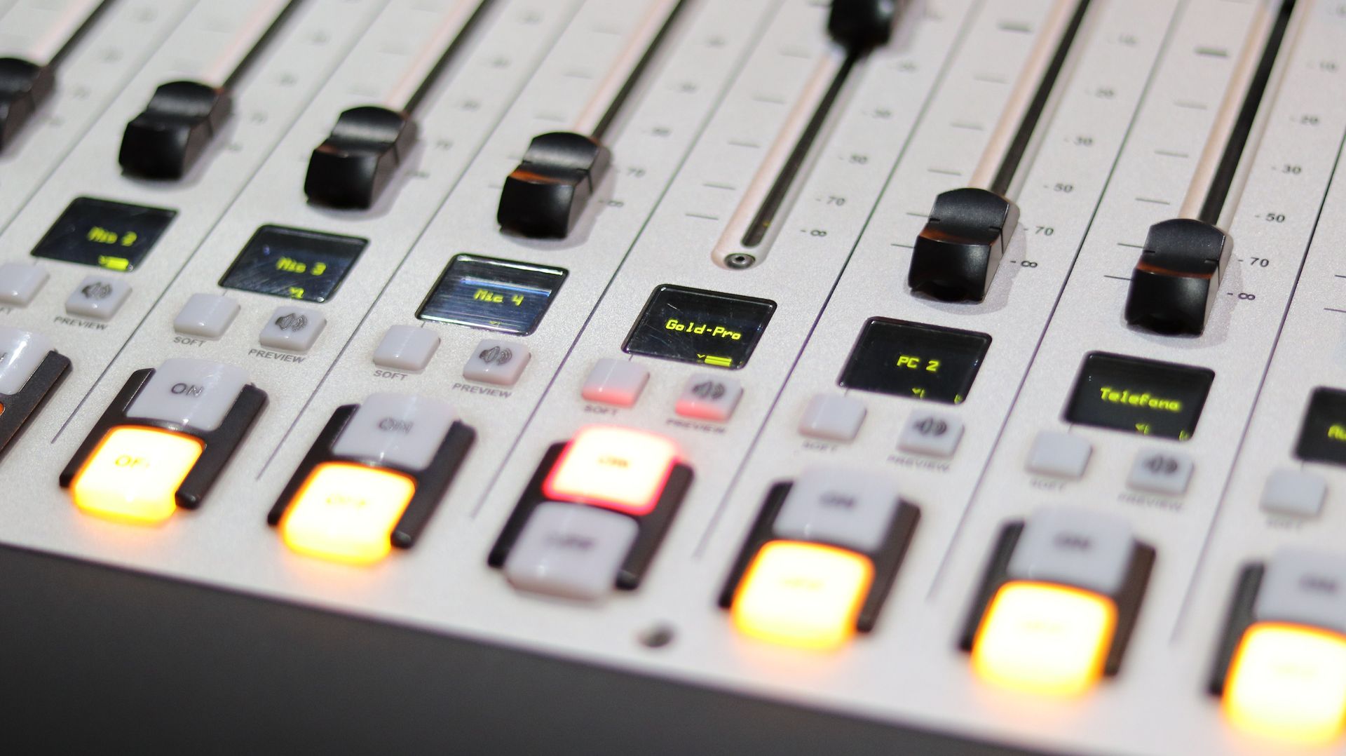 A detailed close-up shot of a professional audio mixer with controls and illuminated buttons.