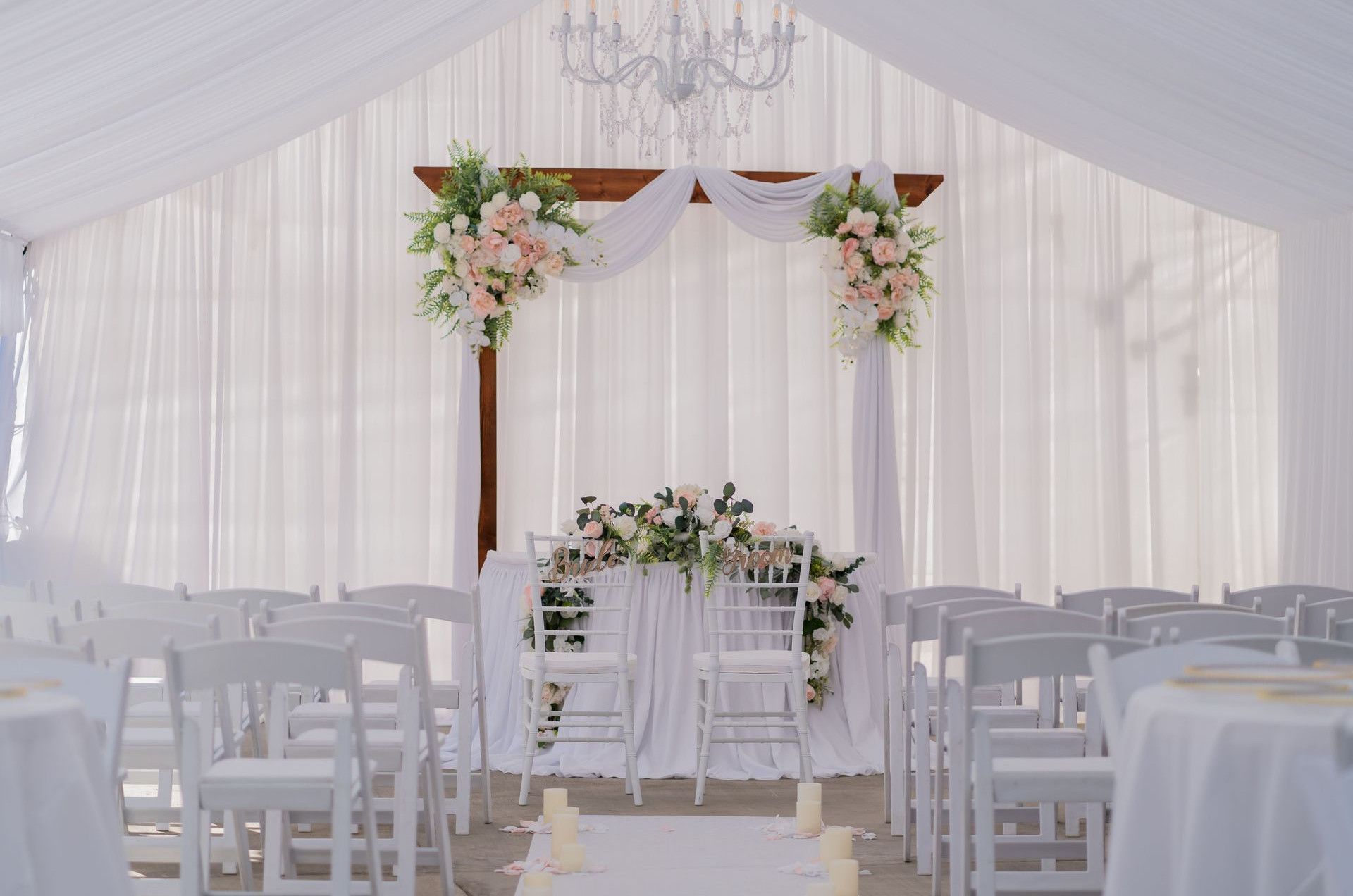 Beautiful wedding ceremony setup with white drapery, floral arrangements, and chandelier. Perfect for elegant nuptials.
